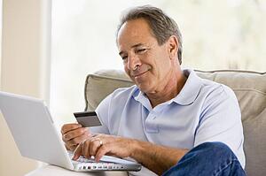 Man in living room with laptop and credit card smiling
