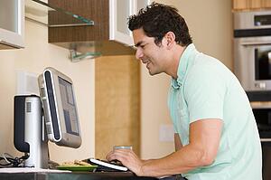 Man in kitchen using computer and smiling