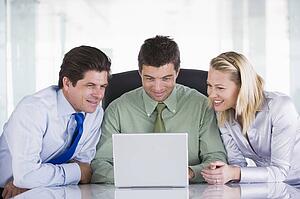Three businesspeople in office with laptop smiling
