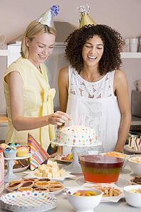 Two women at party putting candles in cake smiling