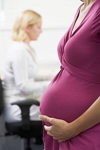 Pregnant woman at work holding belly with coworker in background