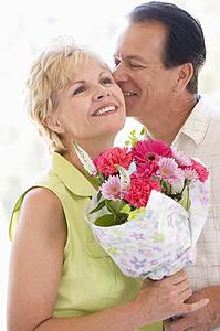 Husband and wife holding flowers kissing and smiling