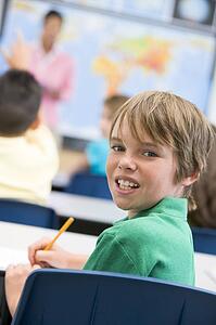 Student in class looking at camera with teacher in background (selective focus)