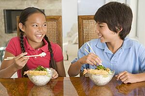 Two young children eating Chinese food in dining room smiling