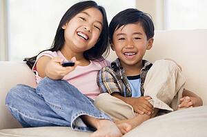 Two youngchildren in living room with remote control smiling