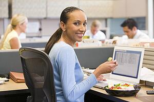 Businesswoman in cubicle with laptop eating salad
