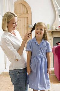 Woman in front hallway brushing young girl's hair and smiling