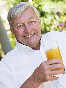 Senior man sitting outdoors with a glass of orange juice