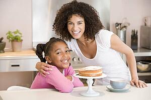 Woman and young girl in kitchen with cake and coffee smiling