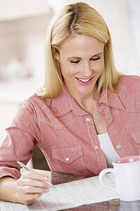 Woman in kitchen with newspaper and coffee smiling