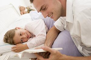 Man reading book to young girl in bed smiling