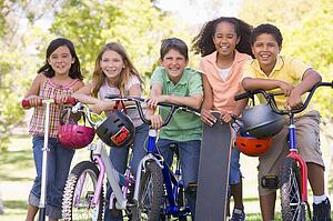 Five young friends with bicycles scooters and skateboard outdoors smiling
