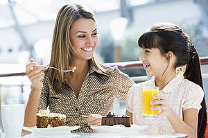 Mother at restaurant with daughter eating dessert and smiling (selective focus)