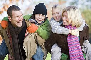 Parents outdoors piggybacking two young children and smiling (selective focus)