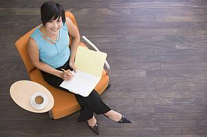 Businesswoman sitting indoors with coffee and folder smiling