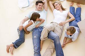Family lying on floor by open boxes in new home smiling
