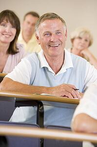 Man sitting in adult classroom laughing with students in background (selective focus)