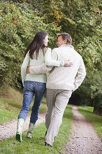Couple walking outdoors on path in park smiling (selective focus)