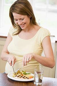 Pregnant woman in kitchen eating chicken and vegetables smiling