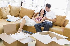 Couple relaxing with champagne by boxes in new home smiling