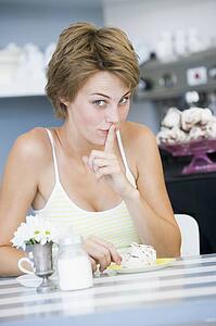 Young woman sitting at a table drinking tea and eating a sweet treat