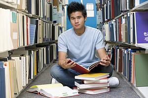 Man sitting on floor in library holding book