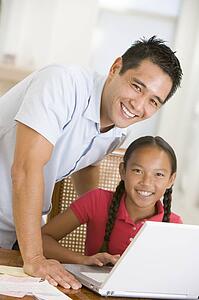 Man and young girl with laptop in dining room smiling