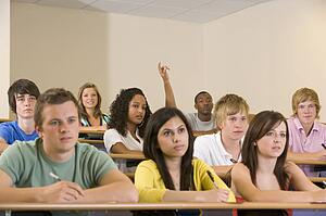 Students in class paying attention and taking notes with one volunteering (selective focus)
