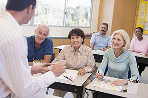 Adult students in class drawing pictures with teacher in foreground (selective focus)