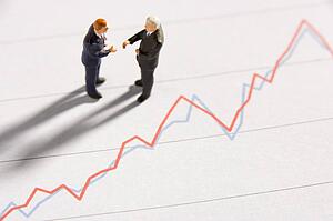 Figurines Of Two Businessmen Shaking Hands On A Line Graph
