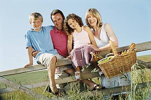 Family outdoors by fence with picnic basket smiling