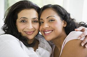 Two women in living room embracing and smiling (high key)