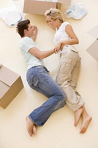 Couple lying on floor by open boxes in new home smiling