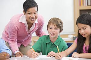 Students in class writing with teacher helping