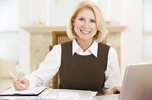 Woman in dining room with laptop and paperwork smiling