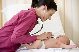 Doctor giving checkup with stethoscope to baby in exam room