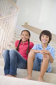 Brother And Sister Sitting On A Stairwell At Home