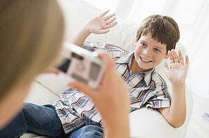 Young girl taking picture of smiling young boy with camera phone indoors