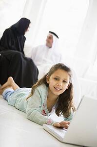 Daughter in living room using laptop and smiling with parents in background (high key/selective focus)