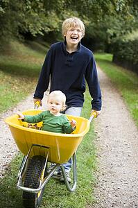 Young boy pushing baby brother in wheelbarrow