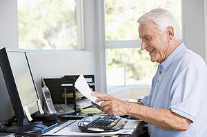 Man in home office with computer and paperwork smiling
