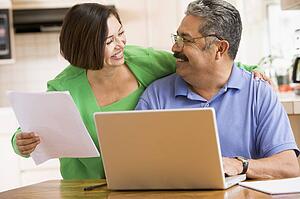 Couple in kitchen with laptop and paperwork smiling