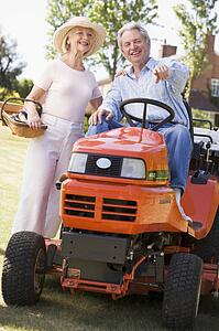 Couple outdoors with tools and lawnmower pointing and smiling