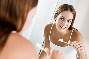 Woman in bathroom brushing teeth and smiling