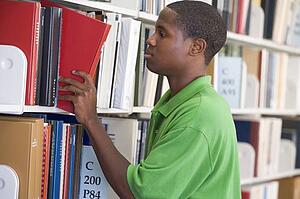 Man in library pulling book off a shelf (depth of field)