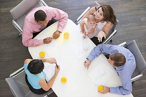 Four businesspeople in boardroom with one holding a baby smiling