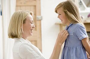 Woman in front hallway fixing young girl's dress and smiling