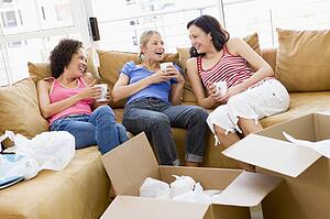 Three girl friends relaxing with coffee by boxes in new home smiling