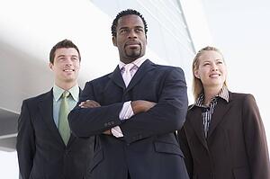 Three businesspeople standing outdoors by building smiling