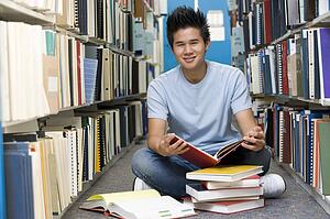 Man sitting on floor in library holding book